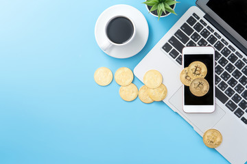 Naklejka premium Stylized clean blue office working desk with bitcoin, smartphone, laptop and coffee cup, workspace design, mock up, top view, flat lay, copy space, close up