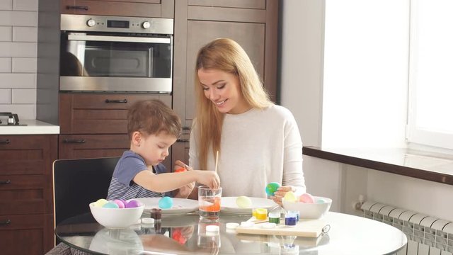 Mother and son paint eggs. Family sitting in a kitchen. Preparing for Easter. Family happiness and Easter celebration concept.