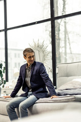 Fancy personable male being seated on bed presented in shop