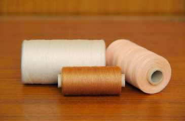 Fototapeta na wymiar spools with white, brown and ochre threads on the table