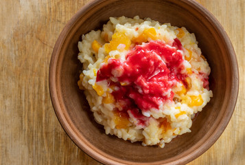Top view on a earthenware bowl with boiled rice cooked in milk with sultana, pieces of pumpkin and flavoured with fresh raspberry juice and honey
