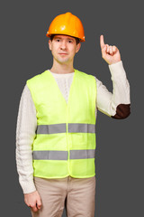 The man the builder in a helmet and a vest points a finger up