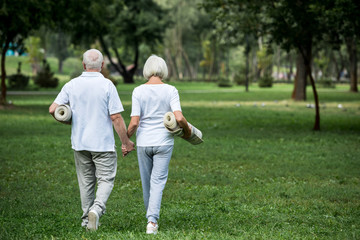 Fototapeta premium senior couple holding fitness mats while walking in park and holding hands