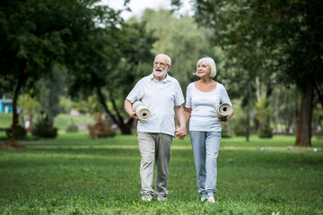 happy senior couple walking in park and holding fitness mats