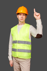 The man the builder in a helmet and a vest points a finger up