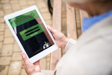 selective focus of senior woman using digitale table with booking on screen