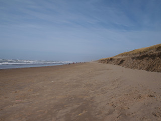 Fototapeta na wymiar view down the beach of Katwijk with distant people. Noordwiijk at the horizon