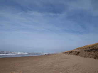 Fototapeta na wymiar view down the beach of Katwijk with distant people. Noordwiijk at the horizon