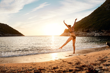 A woman jumping for joy on the seashore at sunset