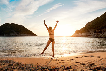 Fototapeta na wymiar A woman jumping for joy on the seashore at sunset