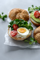 Bagel sandwiches with cream cheese, avocado, tomatoes, egg and greens on gray wooden background. Selective focus. Healthy eating or vegetarian food concept