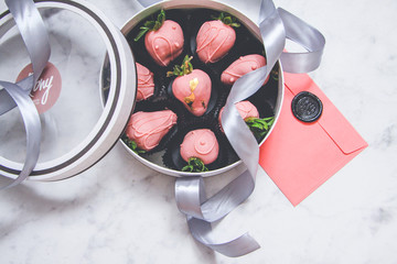 Chocolate-covered strawberries in a gift box with a transparent lid and a gray ribbon and envelope...