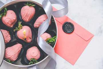Chocolate-covered strawberries in a gift box with a transparent lid and a gray ribbon and envelope...