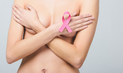 Fototapeta na wymiar midsection view of naked woman with pink breast cancer awareness ribbon, isolated on grey