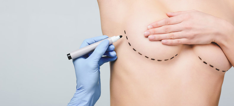 cropped view of plastic surgeon marking lines under breast, isolated on grey
