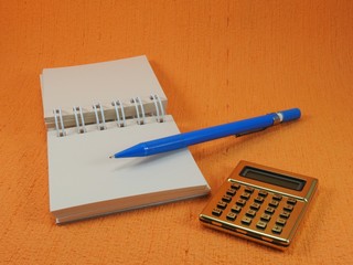 A golden calculator, a small blank notepad and a blue mechanical pencil on an orange surface. The...