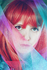 Artistic portrait of a young redhead woman covering by a glitter chiffon