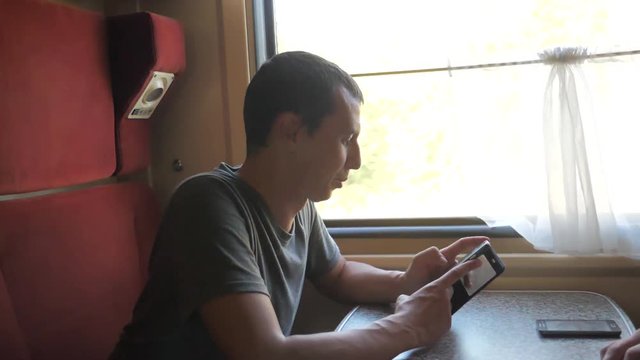 man traveler Relaxing On Train Listening To Music and smiling through the pictures via social media. slow motion lifestyle video. uploading photo using cell phone while riding home by train wagon