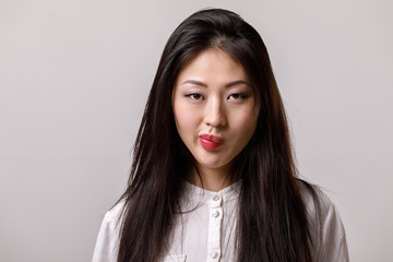 portrait of thinking asian woman in glasses and white shirt on gray background. emotions