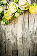 Cold pineapple mojito cocktail with ice, lime and mint, rustic wooden background copy space