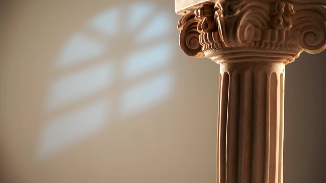 Single ancient corinthian column rotating slowly on bright wall background with window light effect