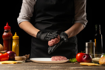 The chef prepares beef patty, with ingredients in the background, restaurant business, fast food,...