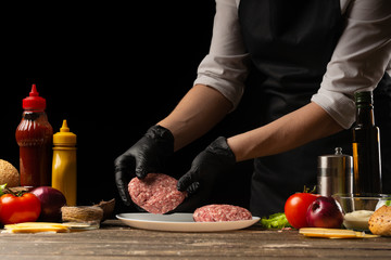 The chef prepares beef patty, with ingredients in the background, restaurant business, fast food, tasty food, gastronomy, cooking, menu