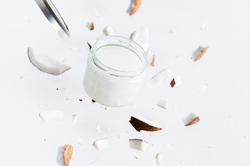 Flying pieces of coconut around coconut butter in glass jar. Exotic levitation concept for cosmetics, spa, perfume, health care products, aroma background with copy space