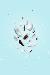 Flying pieces of coconut on blue pastel color. Exotic levitation concept for cosmetics, spa, perfume, health care products, aroma background with copy space