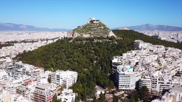Aerial birds eye view video taken by drone of Lycabettus hill and iconic Saint George chapel on top with beautiful scattered clouds, Athens historic center, Attica, Greece