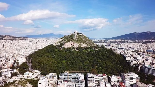 Aerial birds eye view video taken by drone of Lycabettus hill and iconic Saint George chapel on top with beautiful scattered clouds, Athens historic center, Attica, Greece
