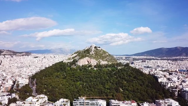 Aerial birds eye view video taken by drone of Lycabettus hill and iconic Saint George chapel on top with beautiful scattered clouds, Athens historic center, Attica, Greece