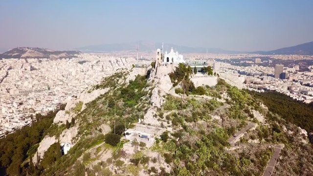Aerial birds eye view video taken by drone of Lycabettus hill and iconic Saint George chapel on top with beautiful scattered clouds, Athens historic center, Attica, Greece