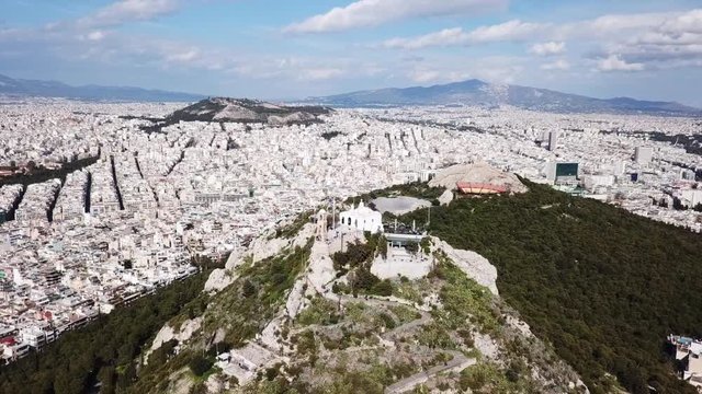 Aerial birds eye view video taken by drone of Lycabettus hill and iconic Saint George chapel on top with beautiful scattered clouds, Athens historic center, Attica, Greece
