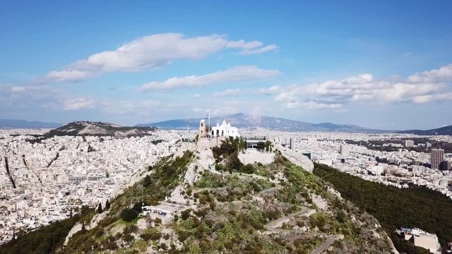 Aerial birds eye view video taken by drone of Lycabettus hill and iconic Saint George chapel on top with beautiful scattered clouds, Athens historic center, Attica, Greece