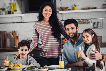 cheerful latin mother hugging cute son and husband near daughter during lunch