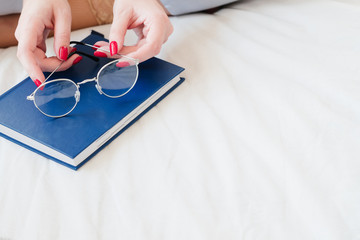 Event planning. Woman hands holding glasses. Closed blue diary. Copy space on ivory background.