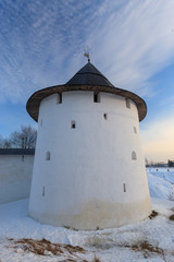 The majestic old Russian tower of white color in the winter against the blue sky with light fluffy clouds