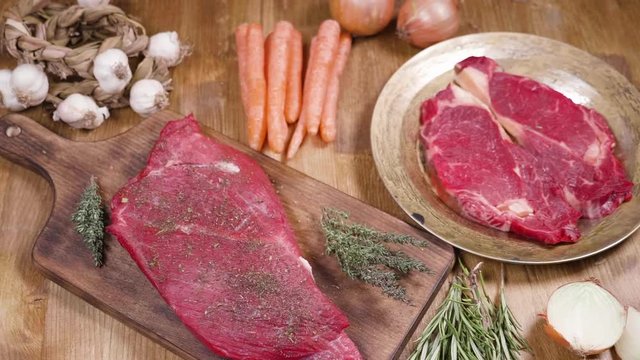 Sliding over a raw ribeye steak and a chunk of raw beef meat. Top view of fresh red meat on a wooden vintage background.