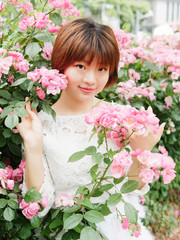 Beautiful young brunette woman in white lace dress looking and smiling in rose garden. Outdoor fashion portrait of glamour Chinese stylish girl. Emotions, people, beauty and lifestyle concept.