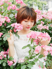 Fototapeta premium Beautiful young brunette woman in white lace dress looking and smiling in rose garden. Outdoor fashion portrait of glamour Chinese stylish girl. Emotions, people, beauty and lifestyle concept.