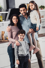 Fototapeta na wymiar handsome latin father holding in arms cute daughter near wife and son at home