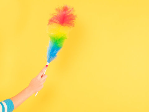 Quality home cleaning. Woman hand with colorful feather duster. Copy space on yellow background.