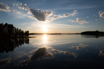 Abendlicht auf ruhigem, schwedischem See mit Wolken- und Sonnenspiegelung