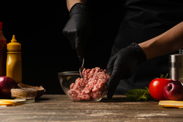 The chef mixes fresh ground beef, to create a burger patty. Against the background with ingredients for a burger. Gastronomy, recipes, menus, fast food. Juicy hamburger