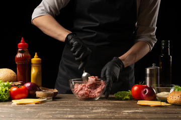 The chef mixes fresh ground beef, to create a burger patty. Against the background with ingredients for a burger. Gastronomy, recipes, menus, fast food. Juicy hamburger