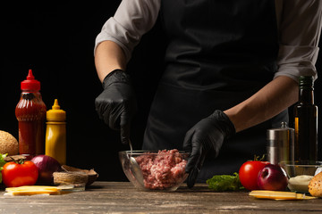 The chef mixes fresh ground beef, to create a burger patty. Against the background with ingredients for a burger. Gastronomy, recipes, menus, fast food. Juicy hamburger