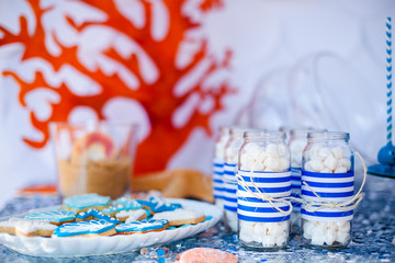 Table with sea décor and plate with sweets, candies, cookies and decorates jars with marshmallow.