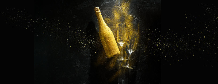 Romantic image of golden champagne bottle, two wine glasses on black stone background