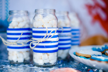 Table with sea décor and plate with sweets, candies, cookies and decorates jars with marshmallow.